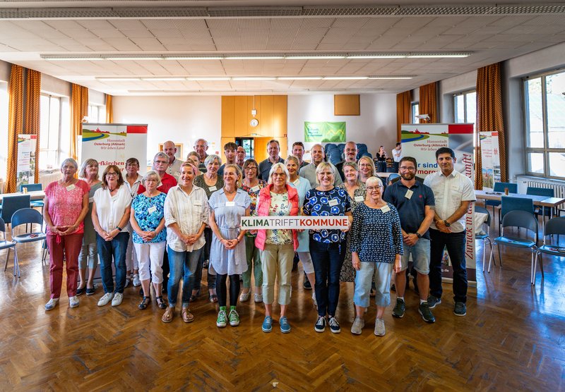 Das Bild zeigt die Mitglieder des Osterburger Bürgerrates bei ihrer Abschlusssitzung am 27. November 2025. Die Mitglieder stehen in drei Reihen; die erste Reihe hält ihre Teilnahmeurkunden in den Händen.  Im Hintergrund sind an der Seite jeweils Flipcharts zu sehen; in der Mitte wird eine Leinwand durch einen Beamer beleuchtet. Dort ist zu lesen: Osterburger Bürgerrat Mobilität.
